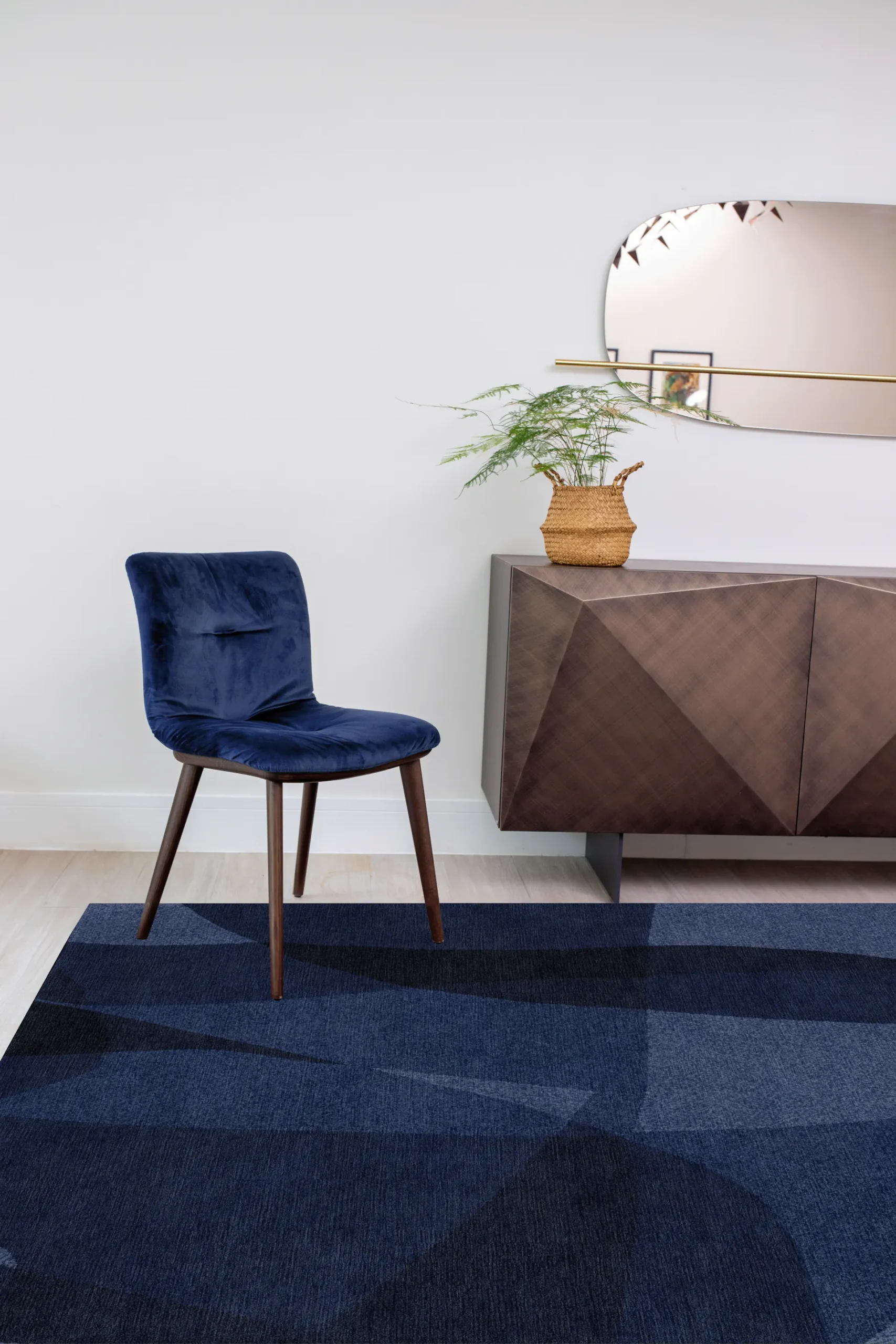 Hand-knotted luxury rug in blue tones with layered tonal movement, styled in a contemporary interior with velvet chair and sculptural sideboard, highlighting depth, warmth and Northwest 35 craftsmanship.